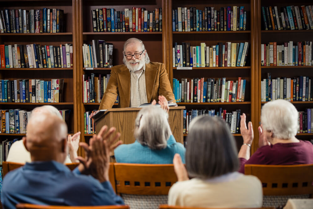 Senior man at a podium giving a lecture to a crowd in a library